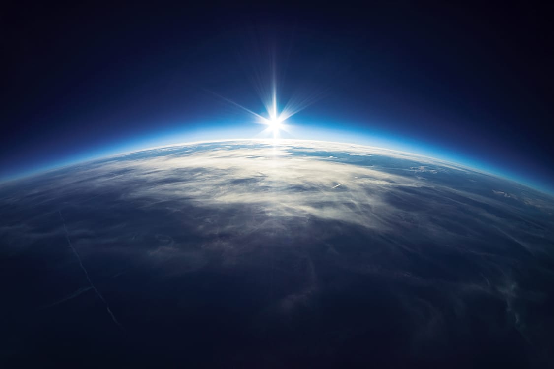 Sunrise over Earth's horizon from space with atmospheric glow.