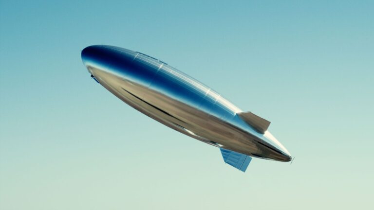 A shiny silver blimp flying against a clear blue sky.