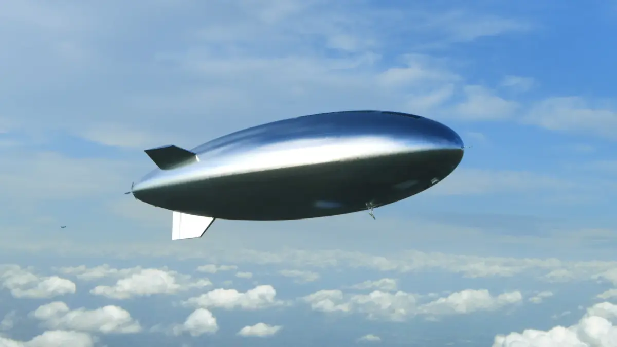 A shiny silver airship flying in a partly cloudy sky.