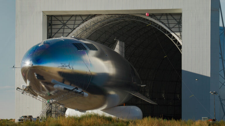 Large silver HAPS airship emerging from hangar