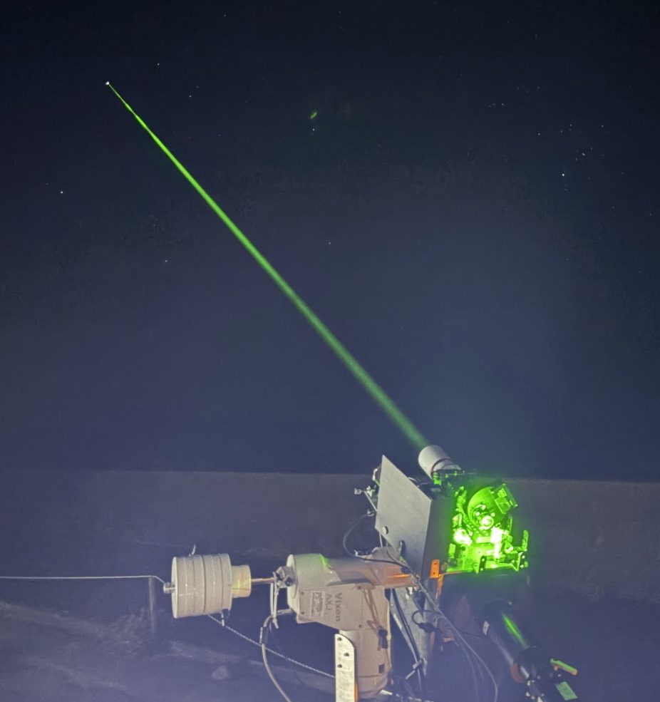 Green laser beam projected into a starry night sky